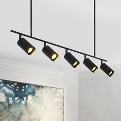 four lights hanging from the ceiling above a painting