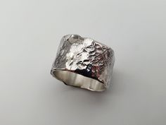 "Introducing \"Lunaris v2\" - a rustic ode to fearless, raw authenticity, etched in a brutalist silver ring / band. It celebrates those unafraid to embrace their rugged and imperfect sides. With its cratered, hammered surface, it embodies the courage of revealing one's true self. (Your act of favouriting not only expresses your style but also graciously inspires me to craft more of what you love. With sincere thanks!) Made from 1.2mm thick, 1.1-1.2 cm wide made from chunky recycled Sterling Silver sheet.  The hammered, and meticulously individually hand-carved surface, evokes an ancient, rugged charm. Each curve and crevice tells a story of patient dedication, rendering every ring unique. It captures the rugged essence of the moon, with occasional smooth areas for contrast. This not only b Silver Hand-forged Wide Band Ring For Anniversary, Brutalist Silver Rings As A Gift, Handmade Silver Brutalist Jewelry, Engraved Sterling Silver Brutalist Jewelry, Handmade Silver Brutalist Rings, Brutalist Hammered Silver Ring, Silver Brutalist Hammered Ring, Jewel Design, Silver Brutalist Hand-cast Rings