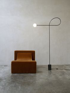 an orange chair sitting in front of a lamp on a cement floor next to a white wall