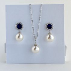 I've created this elegant blue sapphire cubic zirconia and pearl bridal jewelry set in rhodium plated brass setting and the set includes: # Earrings feature large 12mm Swarovski pearls that dangle from brilliant cut blue sapphire cubic zirconia with halo setting 12mm ear stud. Halo setting gives a brilliantly beautiful effect. Total length of the earrings is 2.8 cms. #Classic pearl bridal necklace and pendant set with rhodium plated brass peg and bail. Necklace features a pendant with large 12mm Sapphire Cubic Zirconia Jewelry For Wedding, Sapphire Cubic Zirconia Wedding Jewelry, Formal Pearl Drop Jewelry Sets With Cubic Zirconia, Sapphire Jewelry Sets For Wedding, Elegant Sapphire Jewelry For Wedding, Blue Pearl Drop Wedding Jewelry, Blue Pearl Drop Jewelry For Wedding, Blue Pearl Pendant Jewelry For Wedding, Blue Round Jewelry Sets For Wedding