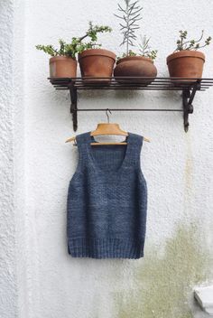 some potted plants are hanging on a shelf above a sweater and tank - top