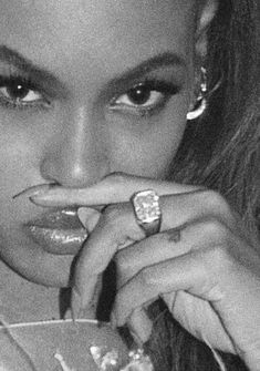 a black and white photo of a woman with her hand on her lip holding a ring