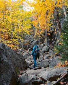 a man hiking up a rocky trail in the woods with fall foliage on either side