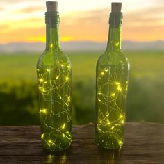 two green bottles with lights in them sitting on a wooden table next to each other