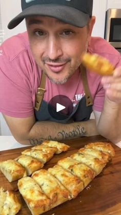 a man in a pink shirt and black hat is holding up some food on a cutting board