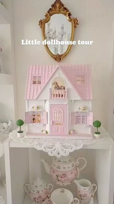 there is a doll house on top of a shelf with cups and saucers in front of it