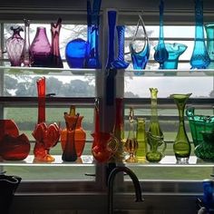 colorful glass vases are lined up on the window sill in front of the sink