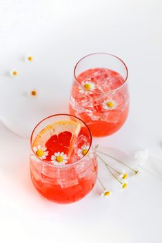 two glasses filled with watermelon and garnished with daisies on a white surface