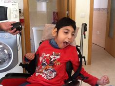 a young boy sitting in a wheel chair with his mouth wide open and tongue out