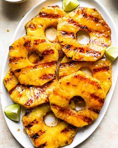 grilled pineapples on a white plate with lime wedges next to them