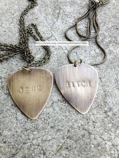 two personalized guitar pick pendants are shown on the ground, one has a name engraved on it