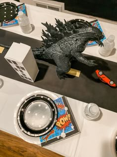 a toy godzilla is sitting on the table with other toys and items around it,