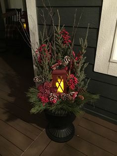 a lantern is lit on the front porch with red berries and pine cones in it