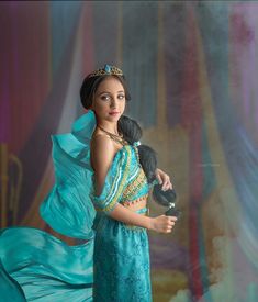 a woman in a blue dress holding a doll and wearing a tiara with feathers on her head