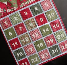 a red and green quilted christmas calendar hanging from a door handle with numbers on it