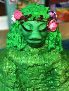 a close up of a green statue with flowers on it's head and eyes