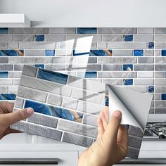 two hands are holding photos in front of a tile backsplash