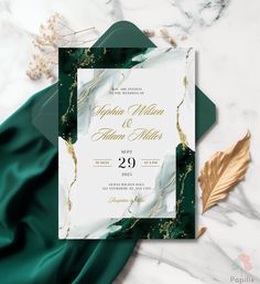 a wedding card with green and gold foil on it, sitting next to a leaf