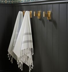 two white towels hanging on the wall next to a towel rack with gold handles and hooks