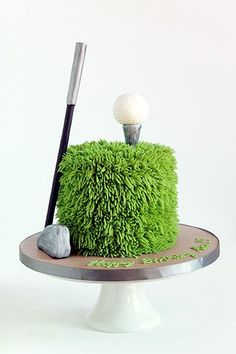 a green cake with a golf ball on top and a tee in the middle, sitting on a plate