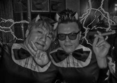 two men in cat ears and bow ties posing for the camera with lightning behind them