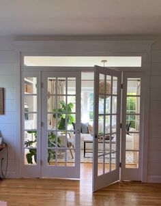 an open door leading into a living room with hardwood floors and white walls, along with potted plants