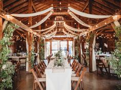 the inside of a barn with tables and chairs set up for a wedding reception in white linens