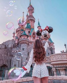 a girl is standing in front of a castle with mickey mouse balloons floating around her