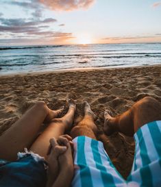 two people are laying on the beach with their feet in the sand as the sun sets