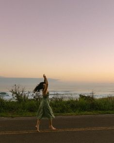 a woman is flying a kite on the road by the ocean at sunset or dawn