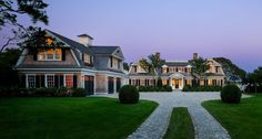 a large house with lots of windows and lights on it's front lawn at dusk