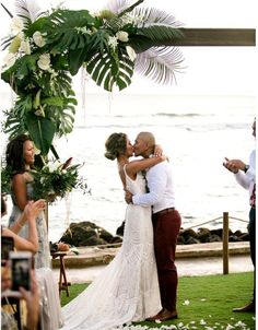 a bride and groom kissing under an arch decorated with flowers at the end of their wedding ceremony