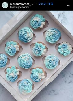 twelve blue cupcakes in a white box on a marble counter top, with frosting swirls