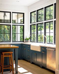 a kitchen with blue cabinets and wooden stools in front of the sink, windows that have black panes on them