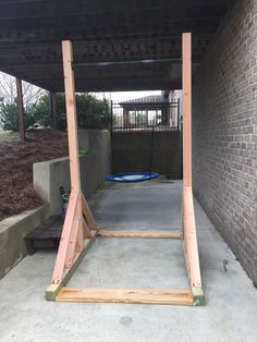 a wooden swing frame in the middle of a walkway under a roof with a blue trampoline