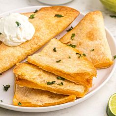 quesadillas on a plate with sour cream and limes in the background