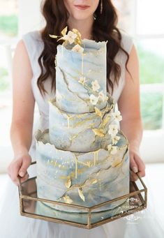 a woman holding a three tiered cake with gold leaf decorations on it's sides