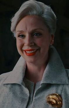 an older woman with white hair and blue eyes smiles at the camera while wearing a gray coat