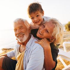 an older man sitting on top of a woman's shoulders next to the ocean