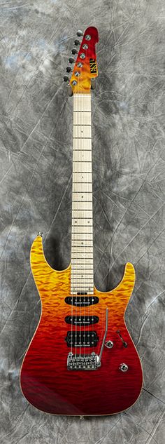 a red and yellow guitar sitting on top of a gray background with an orange neck