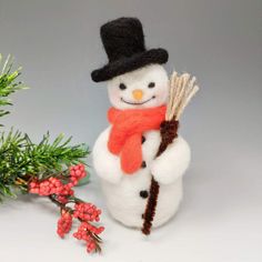 a small snowman with a black hat and scarf holding a broom next to some red berries