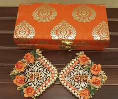 an orange box with two pieces of jewelry in it next to a pair of earrings