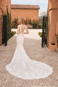 a woman in a white wedding dress standing on a cobblestone walkway looking at the back of her gown