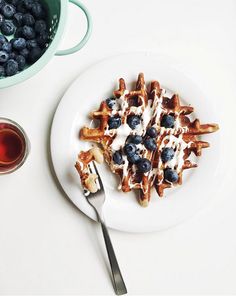 a white plate topped with waffles covered in blueberries next to a cup of tea