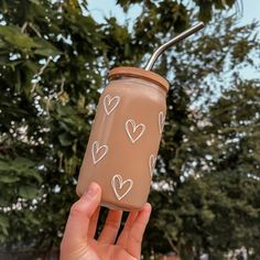 a person holding up a brown cup with hearts painted on it and a straw in the top