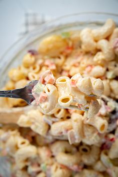 a glass bowl filled with macaroni salad and a spoon full of macaroni