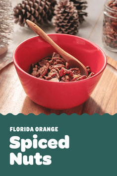 a red bowl filled with spiced nuts on top of a wooden table next to pine cones