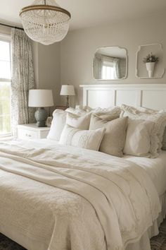 a white bed sitting in a bedroom next to a window with a chandelier