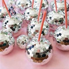 many shiny disco balls are lined up on a pink surface with orange sticks sticking out of them