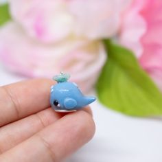 a tiny blue toy whale sitting on top of a persons finger in front of flowers